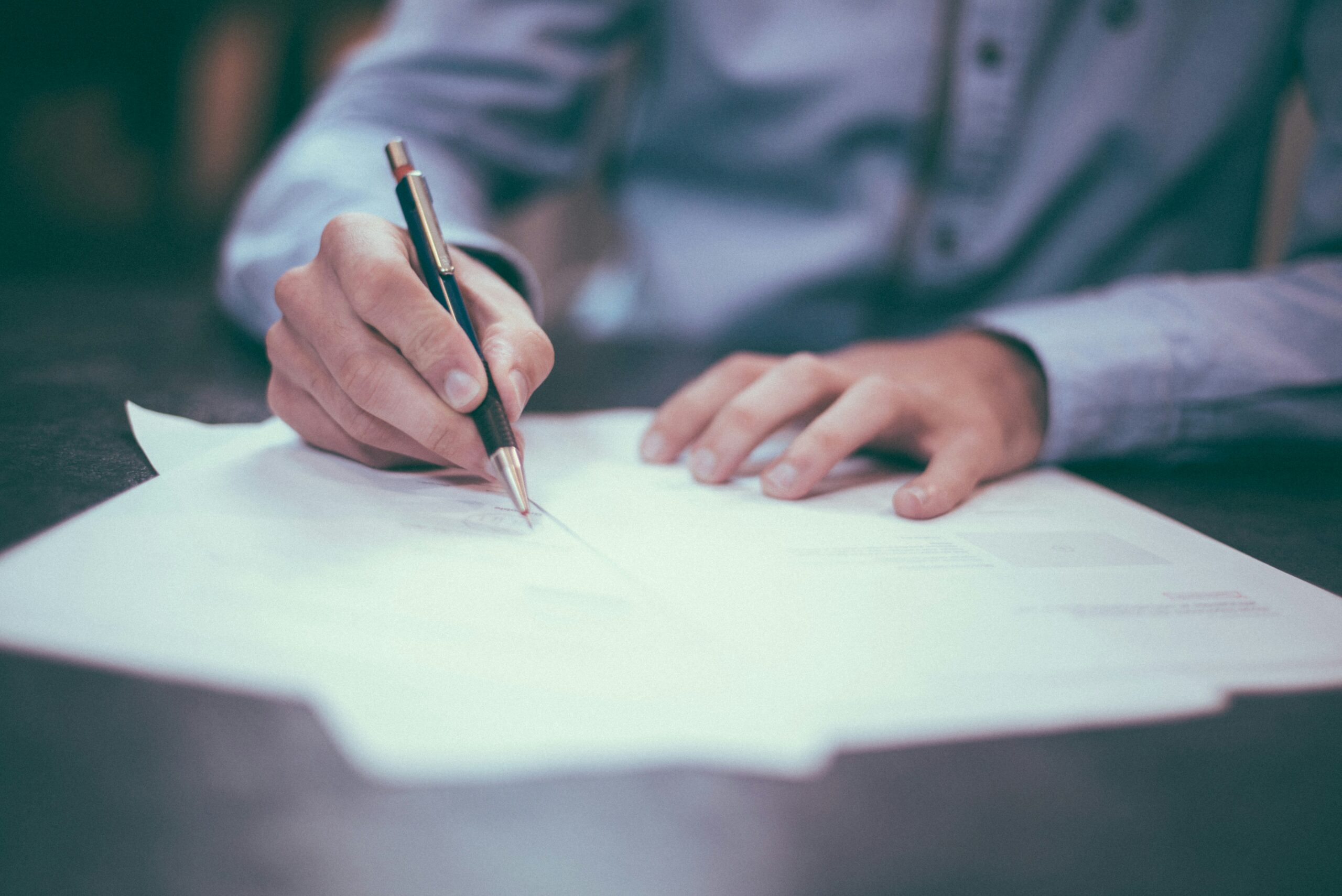 Close-up view of arms of man in light blue business shirt signing policy document with a fancy biro. Showcasing CloudAssist's privacy policy approach, i.e. CloudAssist privacy policy.